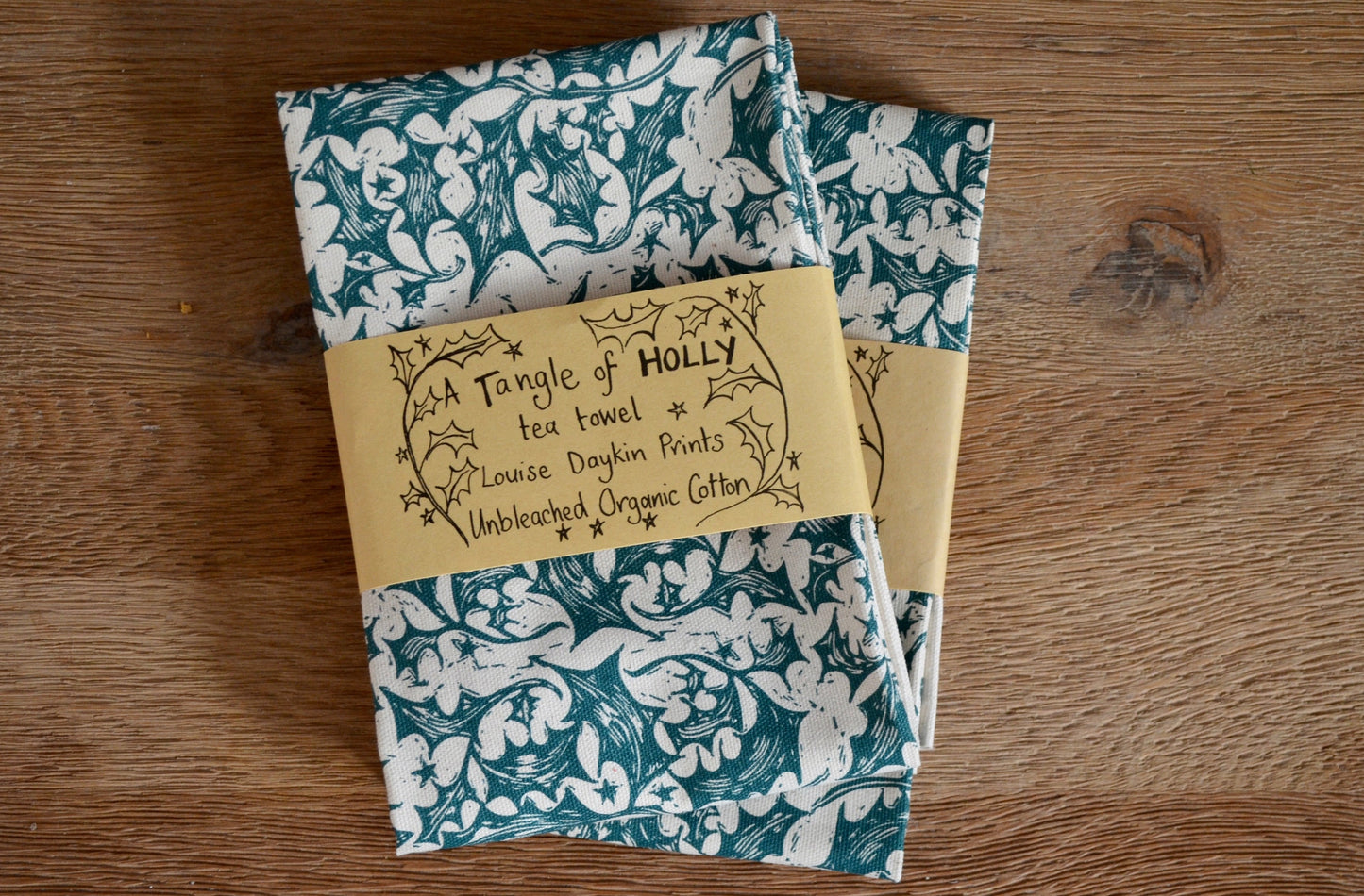 A Tangle of holly tea towel, an unbleached organic off white tea towel with a dark green pattern of holly and stars taken from a lino print design