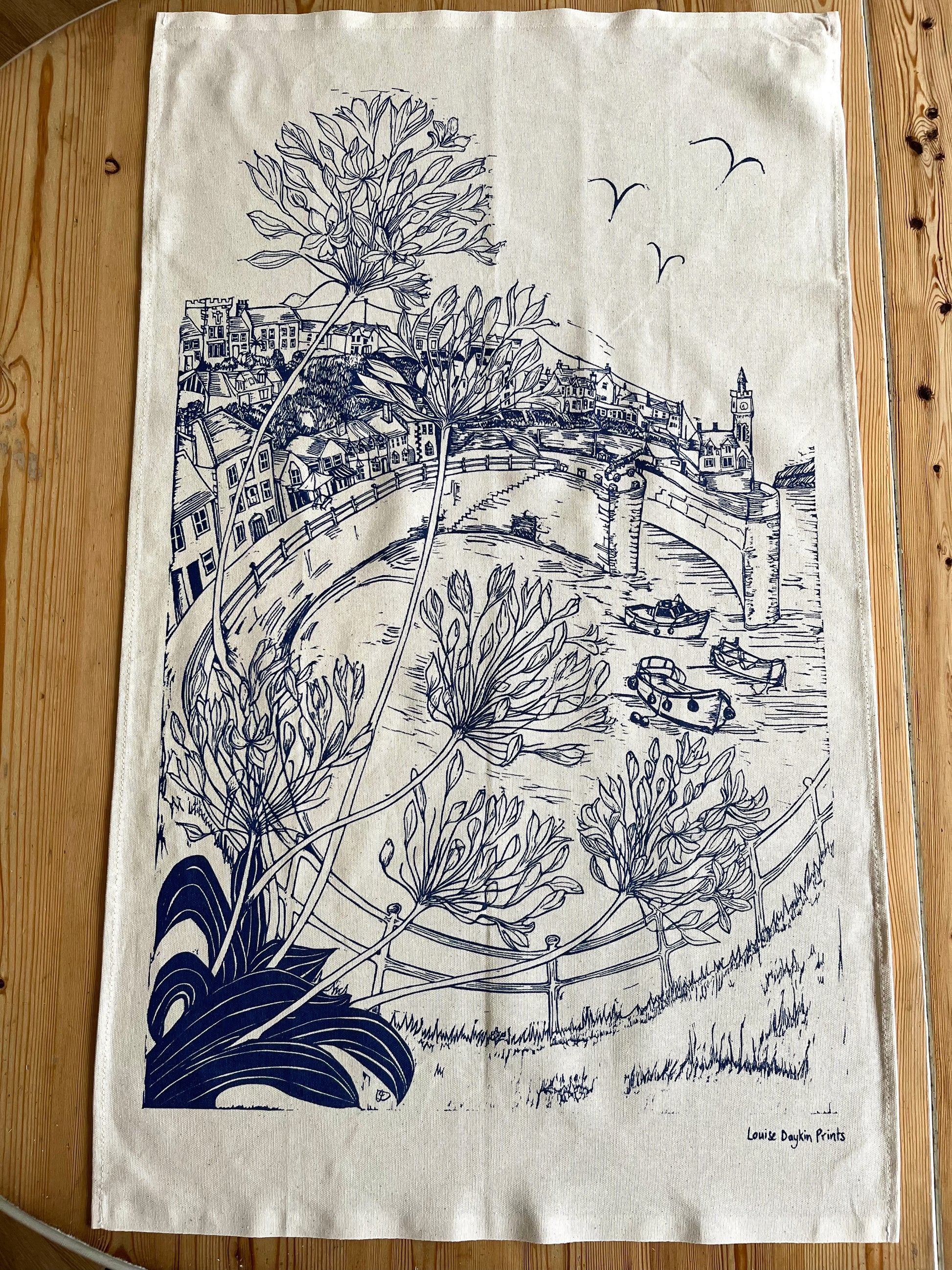 Tea towel with navy illustration Porthleven Harbour in Cornwall with agapathus flowers in the corner