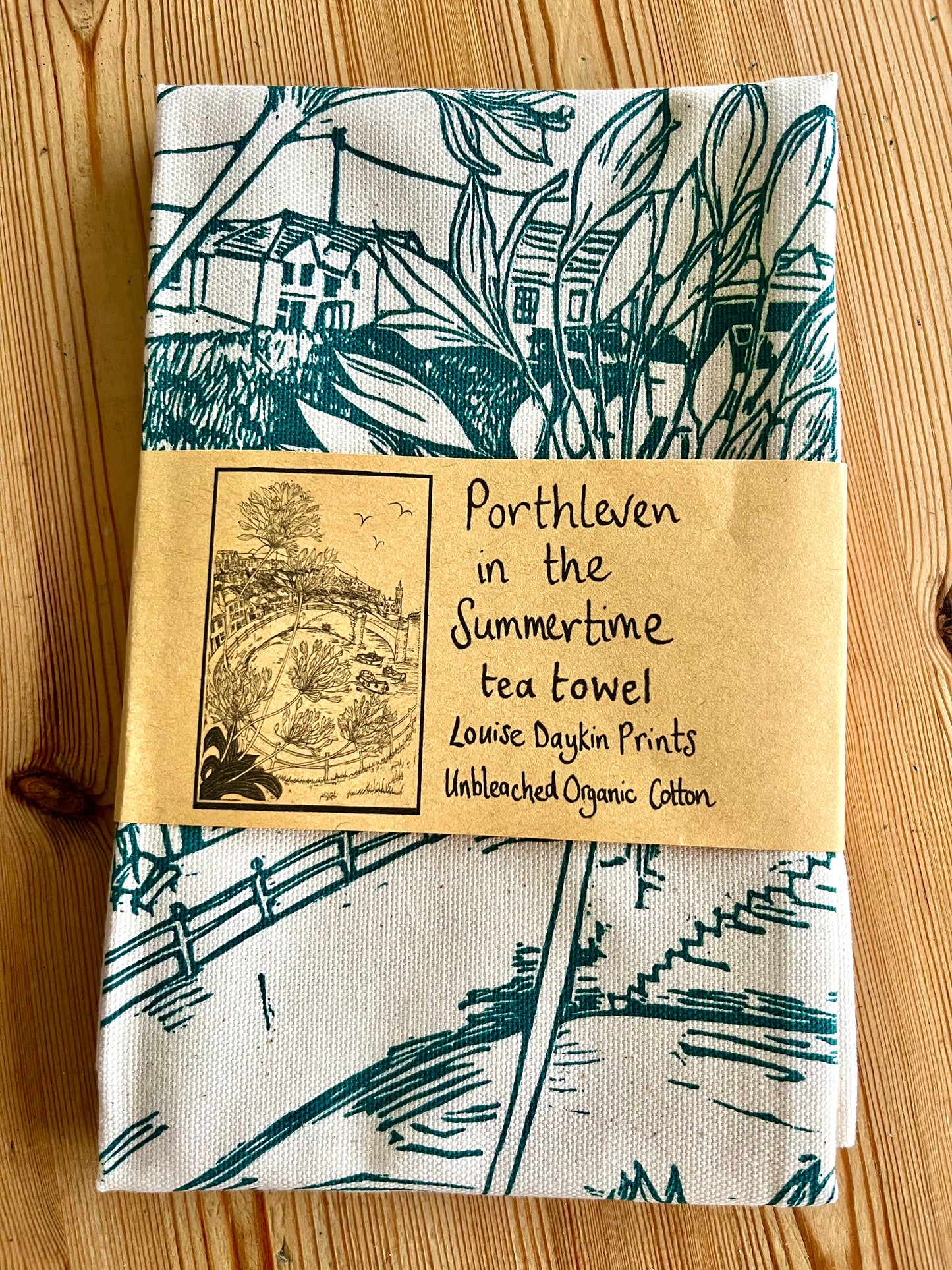 Tea towel with green print showing the "Porthleven in the Summertime" design and packaging 