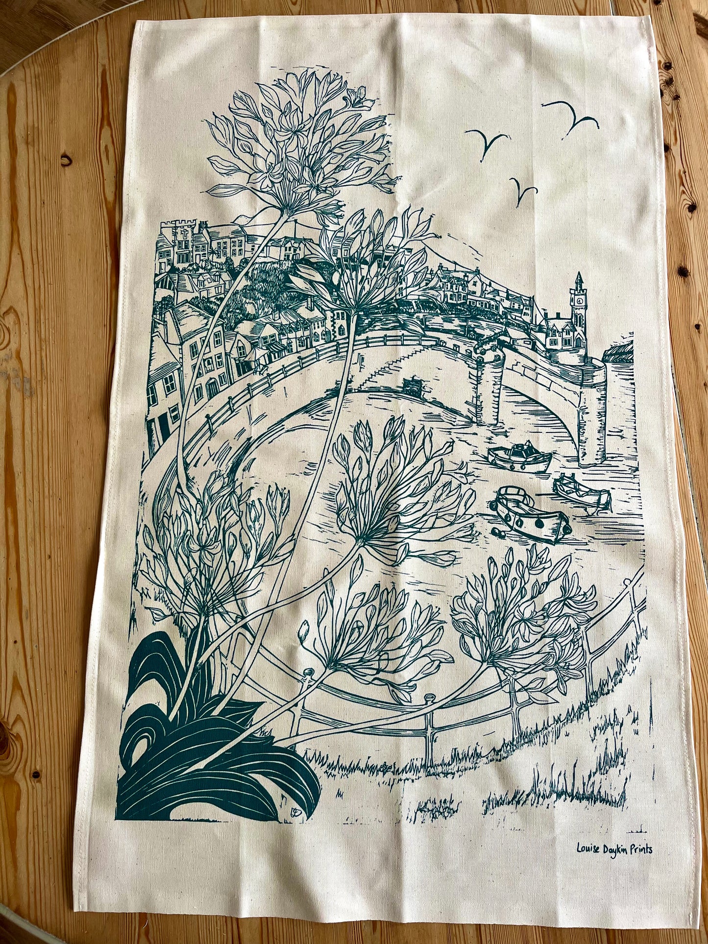 Tea towel with green lino print illustration of a scenic view of Porthleven harbour