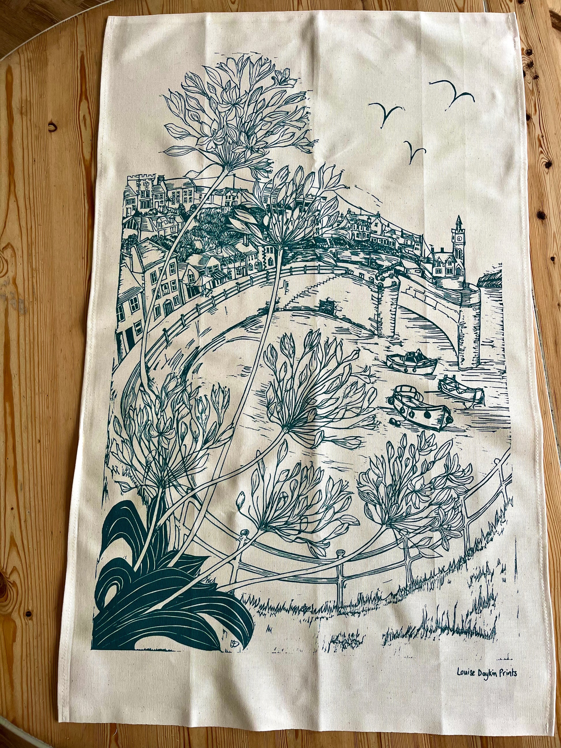 Tea towel with green lino print illustration of a scenic view of Porthleven harbour