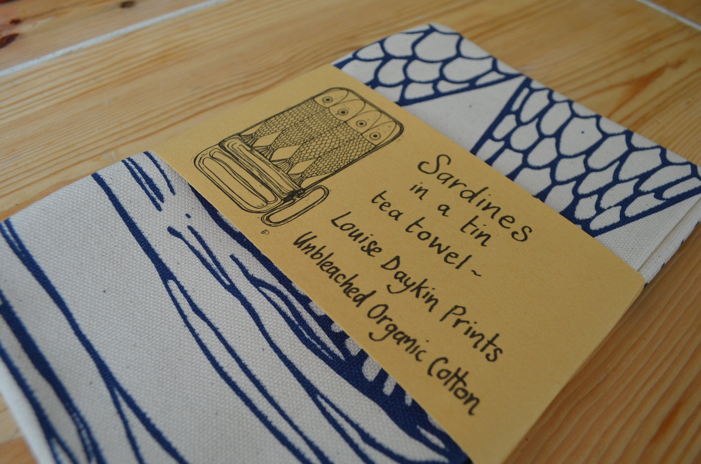 Detail of the packaged "Sardines in a tin" Tea Teatowel with brown paper wrap and handwritten type "Sardines in a tin tea towel, Louise Daykin Prints, Unbleached Organic Cotton
