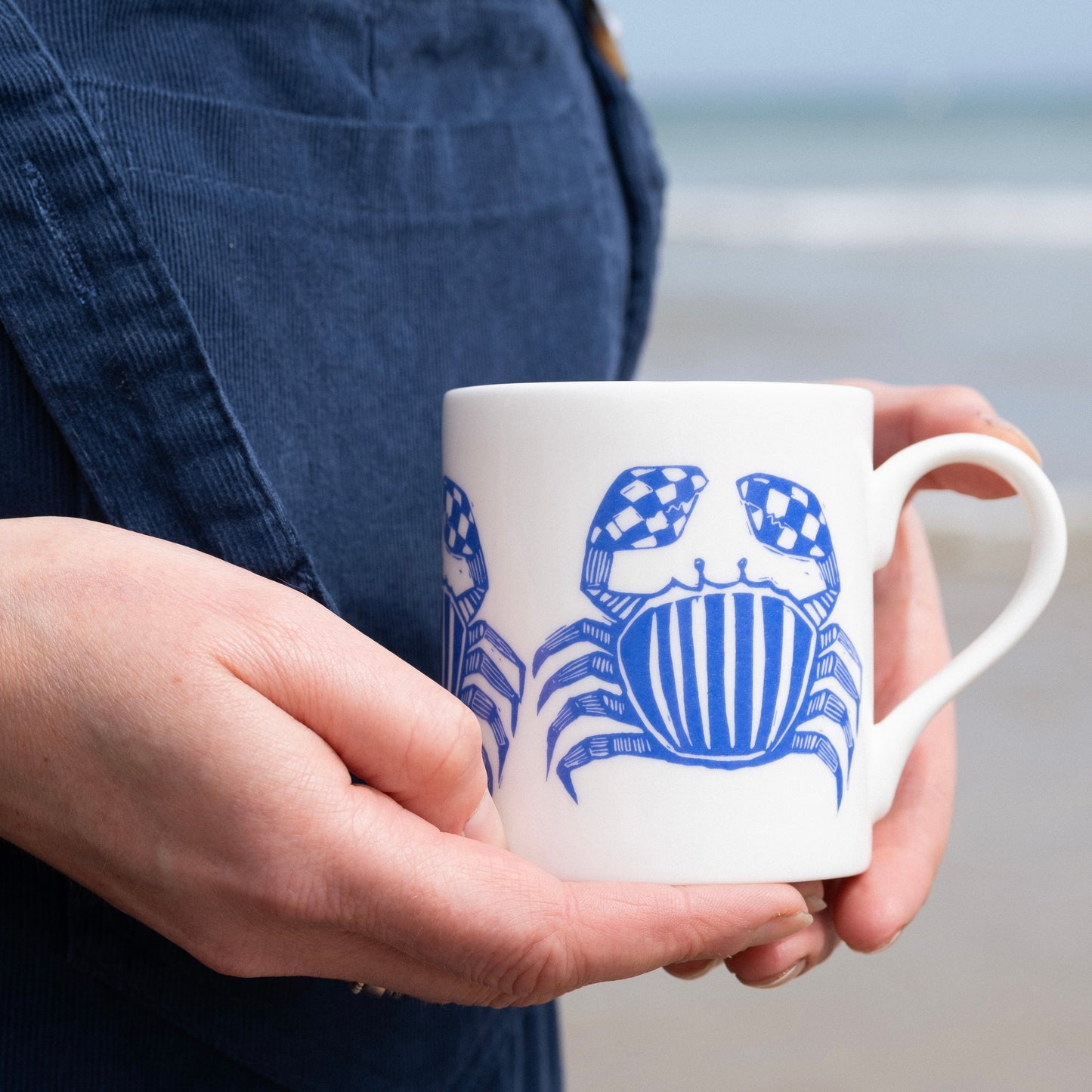 Fine bone china cup with blue crab print, held in hands