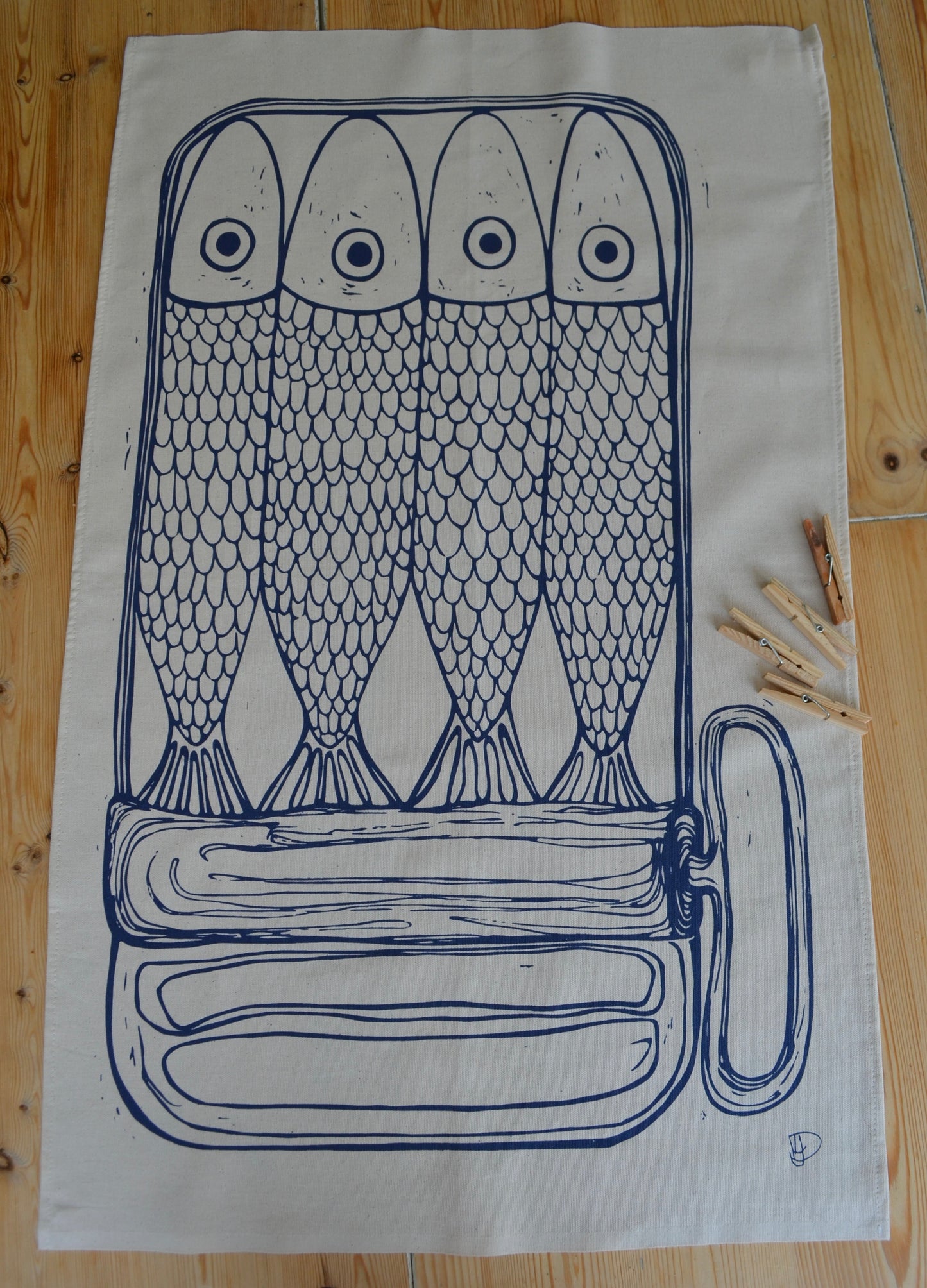 Full image of "Sardines in a tin" tea towel on the kitchen table with pegs to show scale